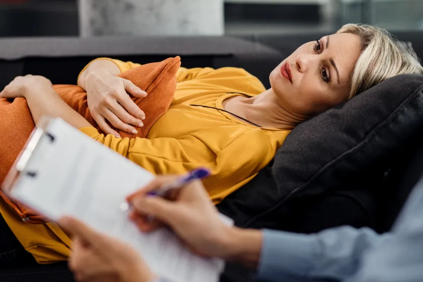 Client relaxing on a couch while a therapist takes notes